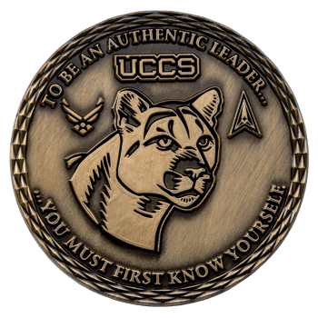 Antiqued bronze challenge coin featuring the UCCS logo, a mountain lion head, Air Force and Space Force insignias, and an engraved leadership quote.