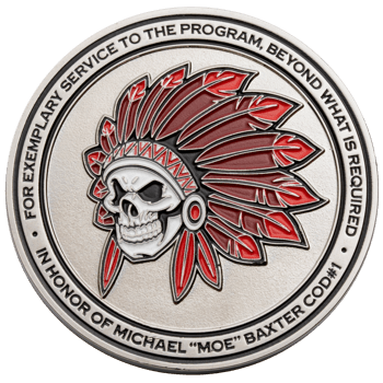Circular silver challenge coin featuring a skull wearing a red and white feathered headdress with text honoring Michael Moe Baxter.