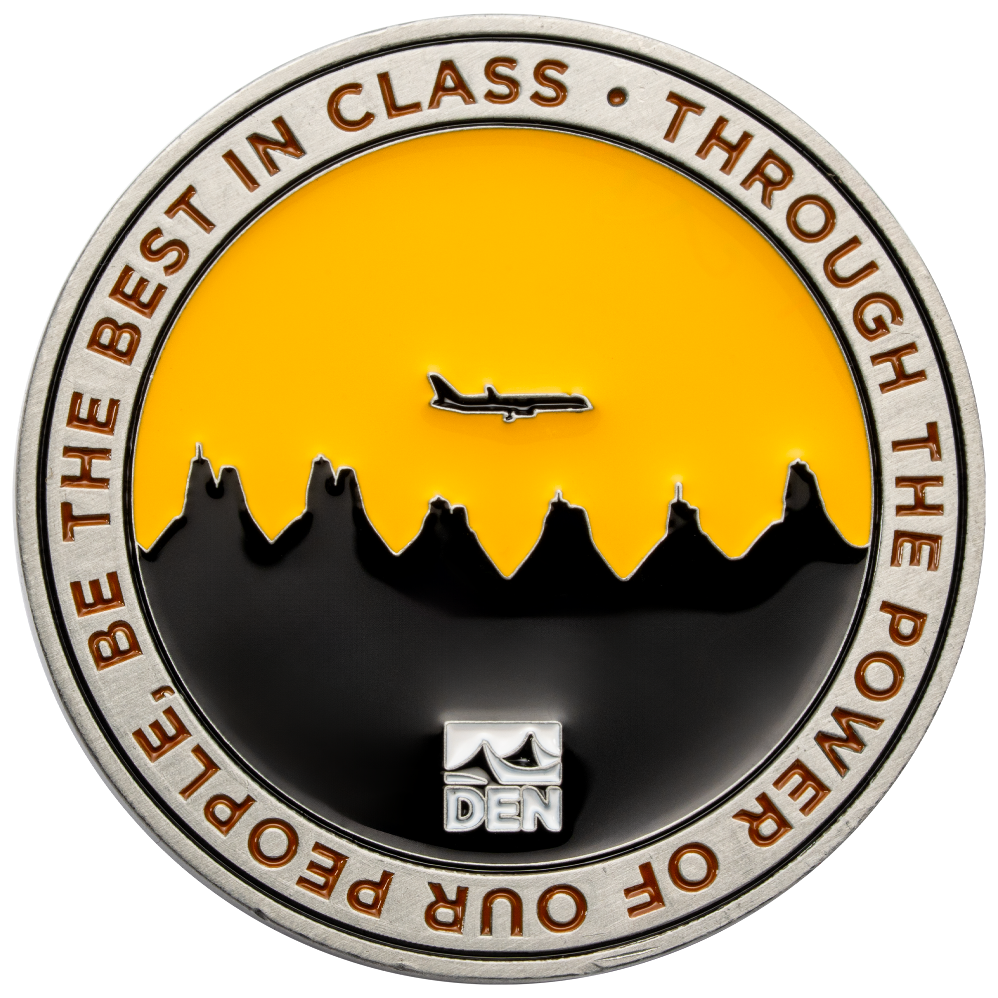 Round challenge coin featuring the DEN logo, a black mountain skyline, and a silhouette of an airplane against a yellow sky.