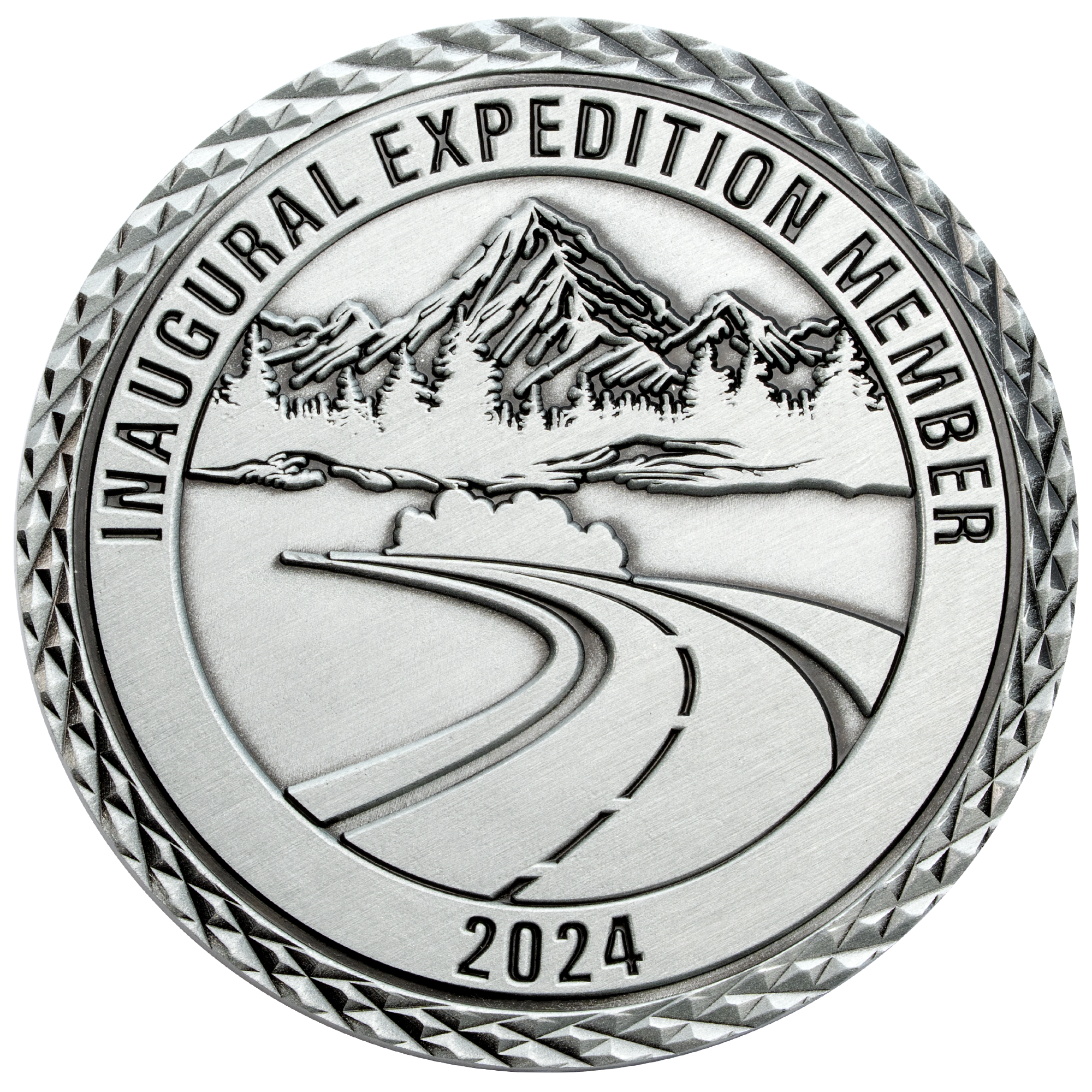 Antique silver challenge coin featuring a mountain range, pine trees, and a winding road with diamond-cut edges.